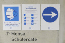 Info zu Maskenpflicht, Corona-Verhaltensregeln und Wegweiser-Pfeilen an Betonwand