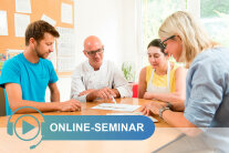 Zwei Männer und zwei Frauen sitzen um Tisch und schauen auf Blatt Papier mit Schriftzug Online-Seminar
