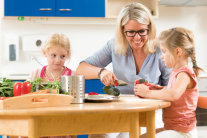Frau bereitet am Tisch mit zwei Kindern Gemüse zu
