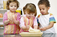 Drei Kinder mit Schürzen vor Teigklumpen auf Holzbrett