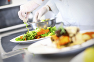 Hände mit Schutzhandschuhen trapieren Salat auf Teller